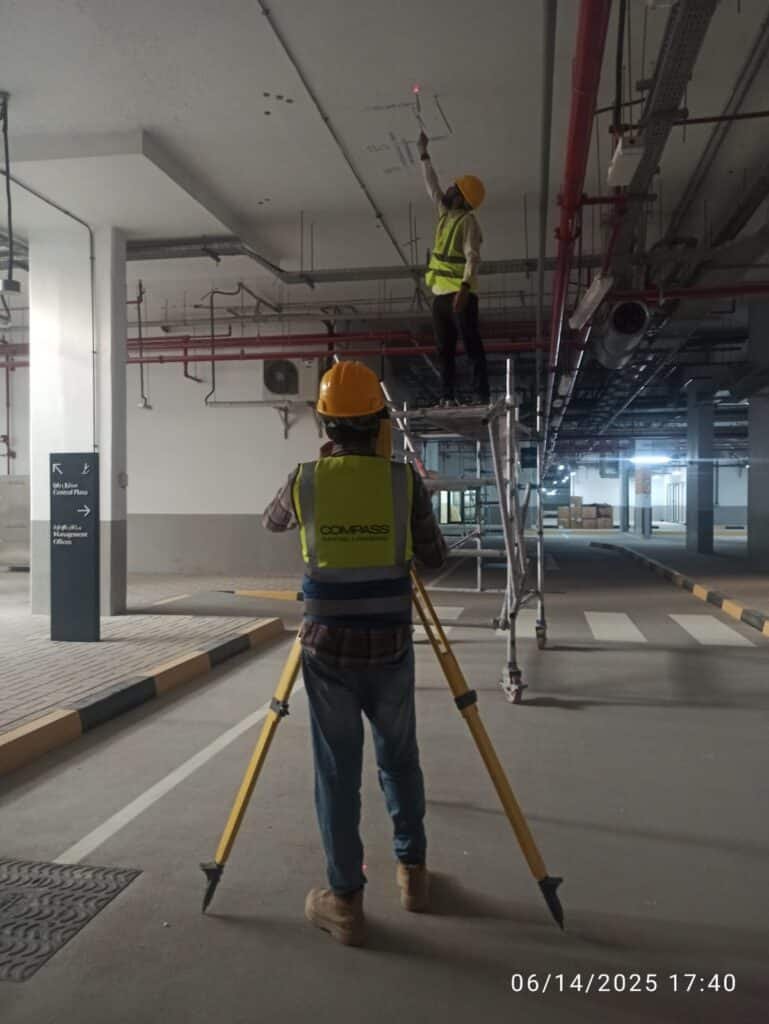 A 3D laser scanner mounted on a tripod with a connected tablet controller, performing a digital scan inside a multi-story concrete building under construction.