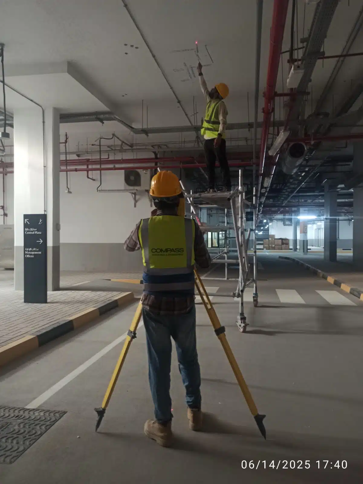 A 3D laser scanner mounted on a tripod with a connected tablet controller, performing a digital scan inside a multi-story concrete building under construction.