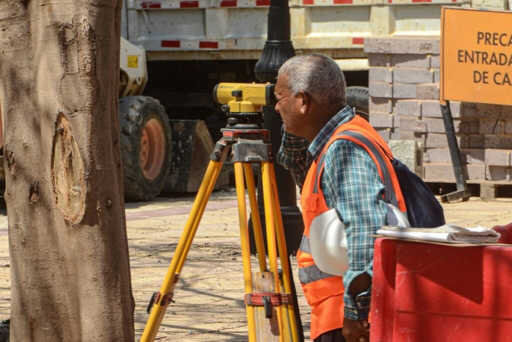A surveyor using a total station on a tripod at a development site